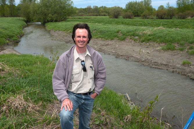 A man standing on the bank of a small river.